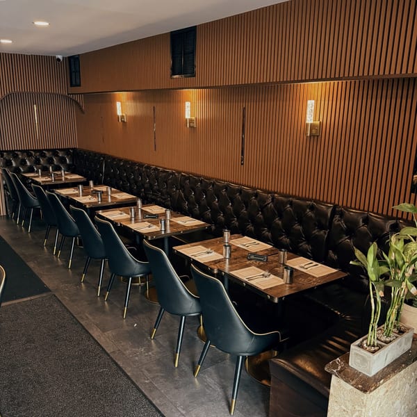 A long row of set tables with black chairs and a tufted leather booth against a wood-paneled wall.