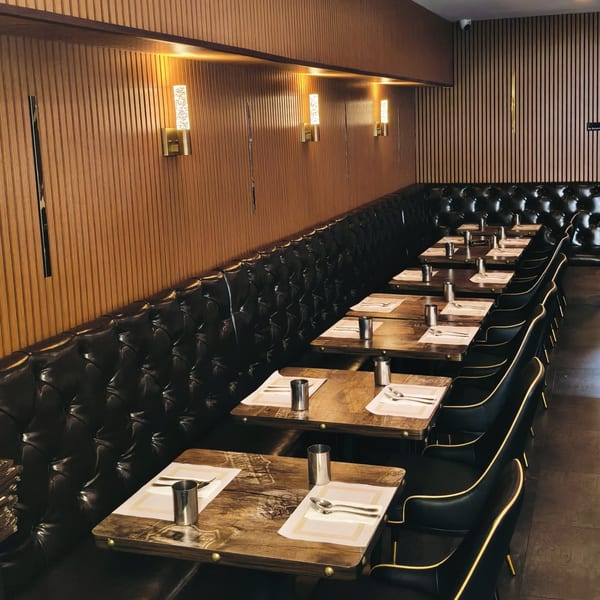 A row of set tables with black leather booth seating and chairs in a restaurant dining room.