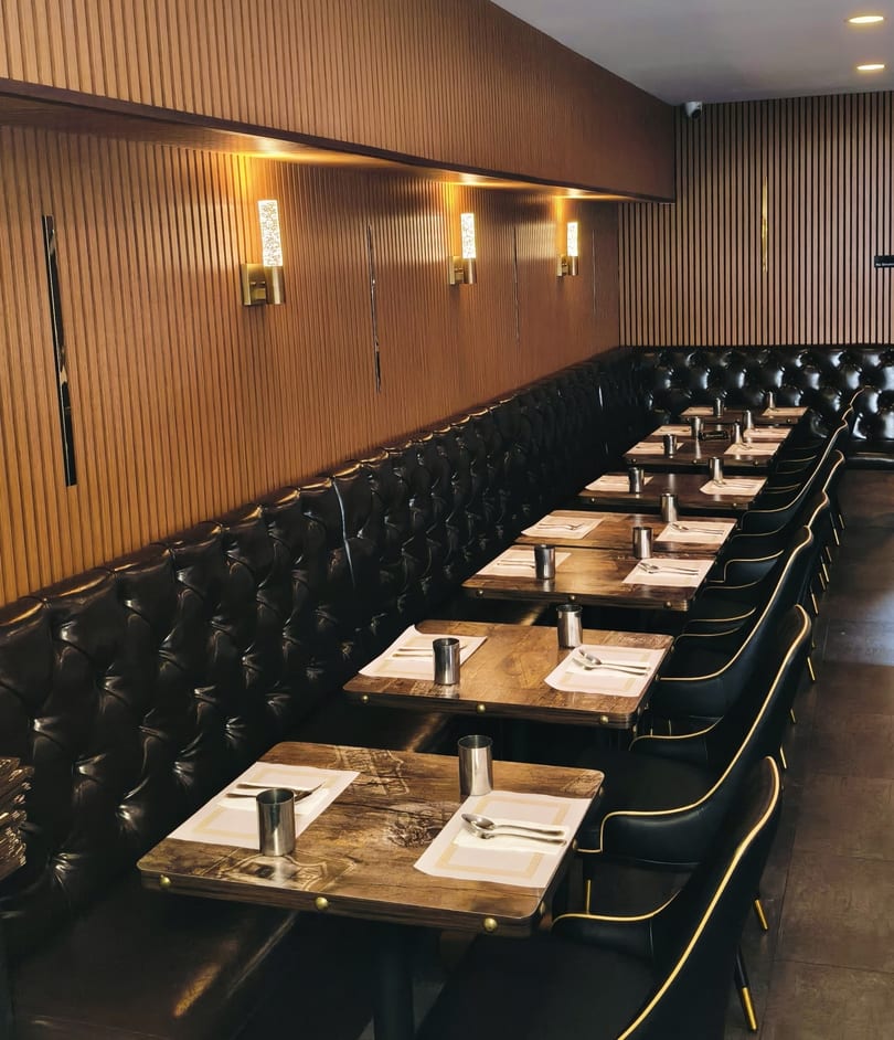 A row of set tables with black leather booth seating and chairs in a restaurant dining room.