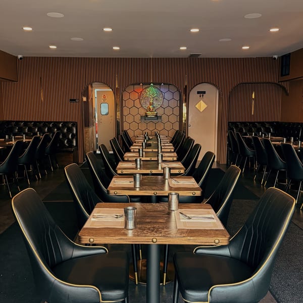 Empty restaurant dining room with rows of tables set with silverware and black chairs.