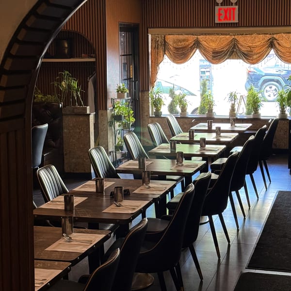 A restaurant dining room with set tables and chairs, seen through an arched doorway.