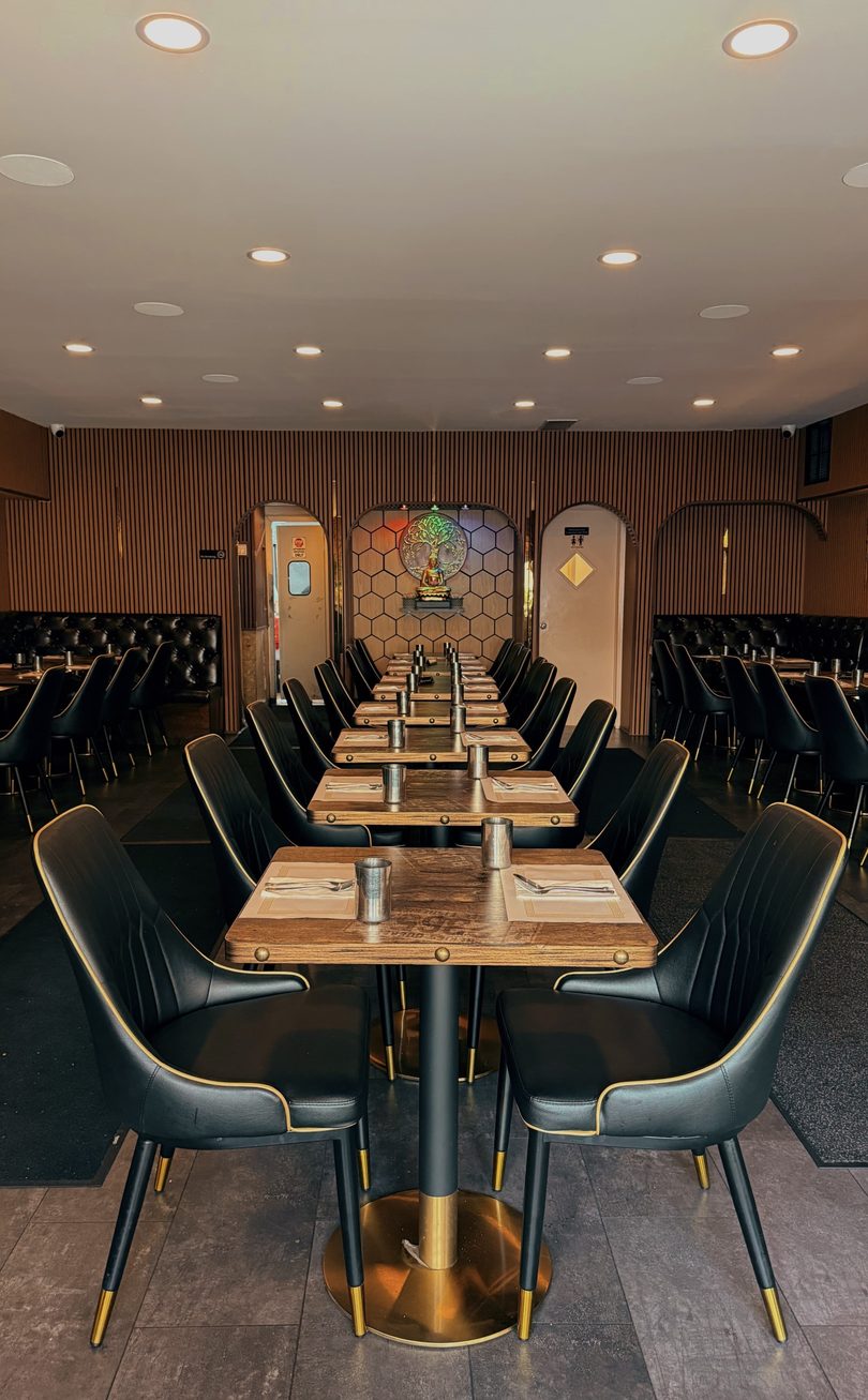 An empty restaurant dining room with rows of tables and black chairs, leading to a Buddha statue.