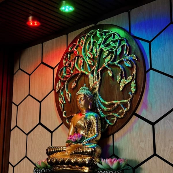 Golden Buddha statue with lotus flowers, illuminated by colorful lights against a wooden tree of life.
